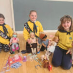 Three girls in the brownies playing with dolls.