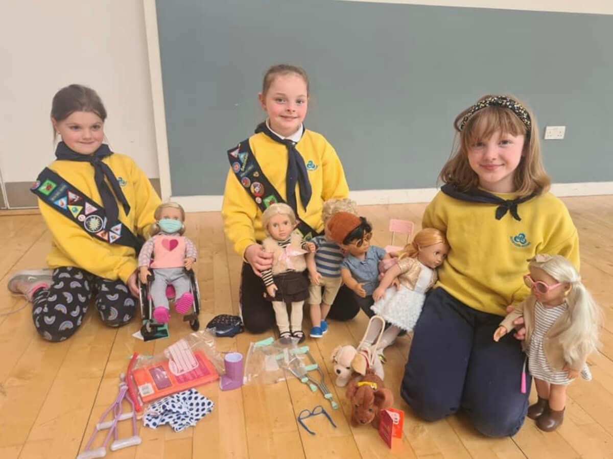 Three girls in the brownies playing with dolls.